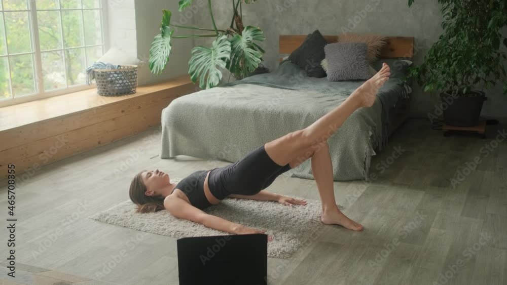 A young woman is engaged in online workouts at home. The laptop is on the floor and the girl goes in for sports on her own.