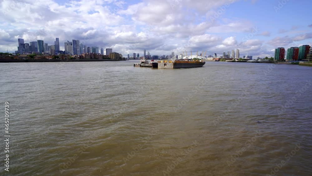 Tilting view revealing East London with Docklands and Canary Wharf on one side and Greenwich and the Millennium Dome on the other. Barges float in the middle of the wide River Thames Tilting view revealing East London with Docklands and Canary Wharf on one side and Greenwich and the Millennium Dome on the other. Barges float in the middle of the wide River Thames