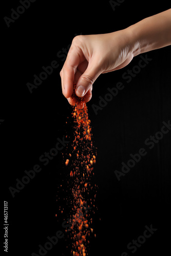 Fototapeta Naklejka Na Ścianę i Meble -  Hand sprinkling cayenne pepper on black background