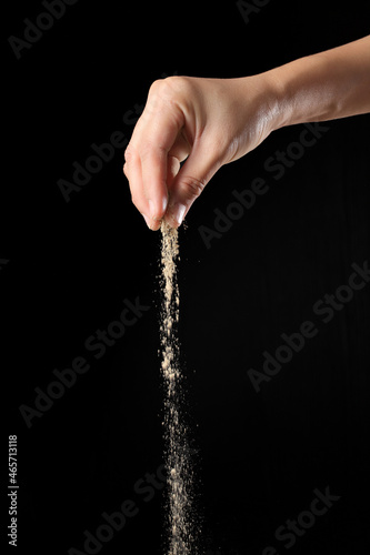 Hand sprinkling ground pepper isolated on black background