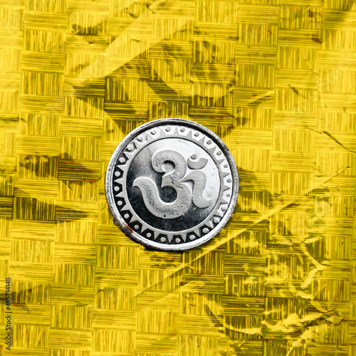 Silver Coin embossing with sacred spiritual symbol Om or Aum on golden backgrounds.