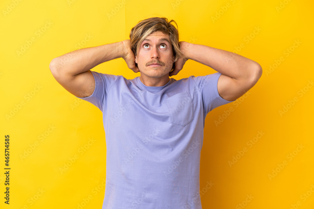 Handsome blonde man isolated on yellow background frustrated and covering ears Handsome blonde man isolated on yellow background frustrated and covering ears
