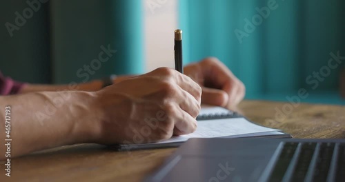 Close-up shot of hands of unrecognizable men writing down in notepad while sitting at cafe table. Slow motion photo