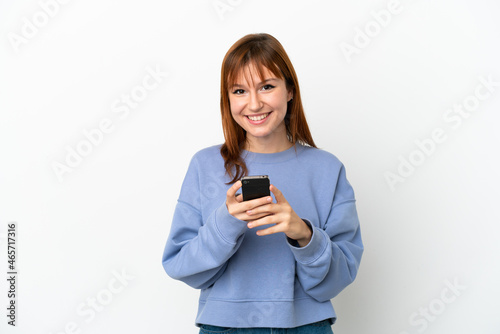 Redhead girl isolated on white background sending a message with the mobile