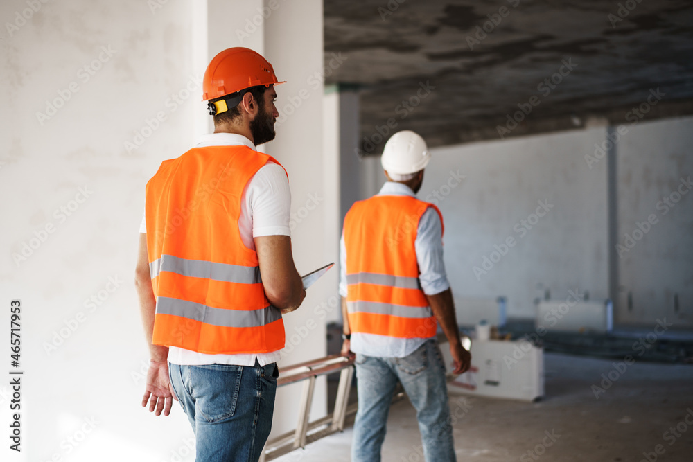 Two young male engineers in uniform and hardhats working at construction site