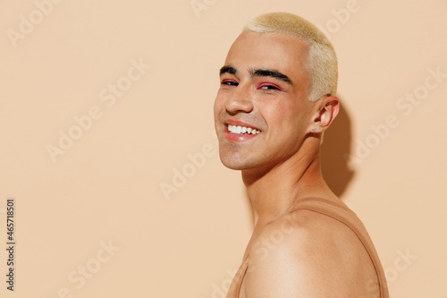 Obraz na plátně Side view young handsome fun smiling blond twink latin gay man 20s with make up in beige tank shirt look camera isolated on plain light ocher background studio portrait People lgbt lifestyle concept