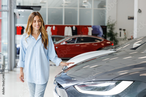 Happy manager woman customer female buyer client in blue shirt walk goign touch car choose auto want to buy new automobile in showroom vehicle salon dealership store motor show indoor. Sales concept. photo