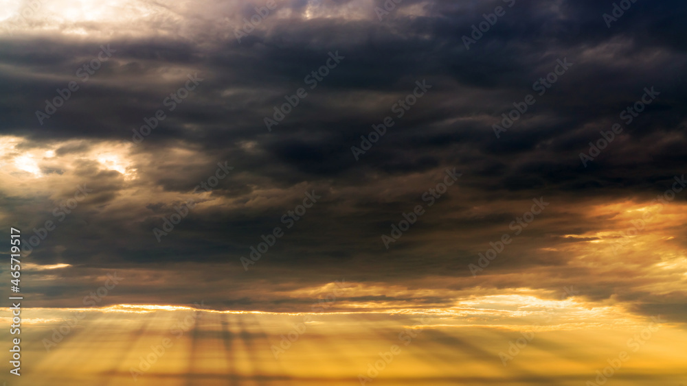 Sun beams or rays breaking through the dark clouds at sunset. Beautiful spectacular conceptual meditation background. Artistic golden sunset edit.