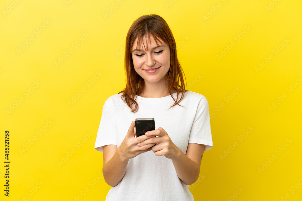 Redhead girl isolated on yellow background sending a message or email with the mobile Redhead girl isolated on yellow background sending a message or email with the mobile