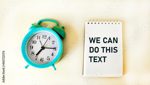 Phrase WE CAN DO THIS TEXT, on notepad and white background with clock © Sviatlana