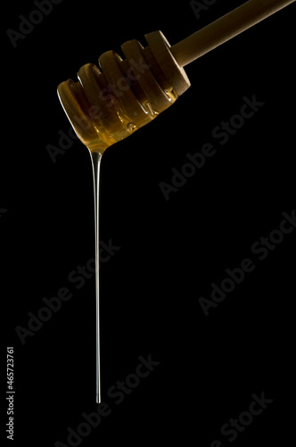 Honey dipper with golden honey dripping off, low key