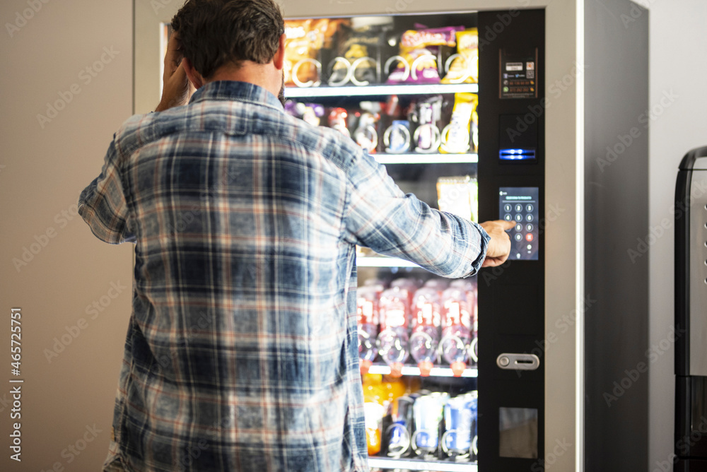 Hipster style man viewed from back buying snacks or drink from vending automatic machine typing product code. People and travel concept lifestyle Hipster style man viewed from back buying snacks or drink from vending automatic machine typing product code. People and travel concept lifestyle