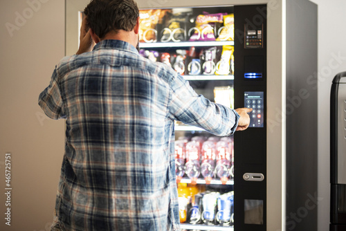 Hipster style man viewed from back buying snacks or drink from vending automatic machine typing product code. People and travel concept lifestyle photo