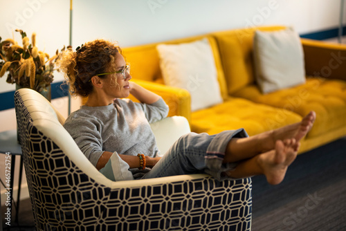 One woman sitting on the chair at home with legs up and barefoot comfort. Female people at home in linving room relax and enjoy resting leisure activity alone. Concept of house and owner photo