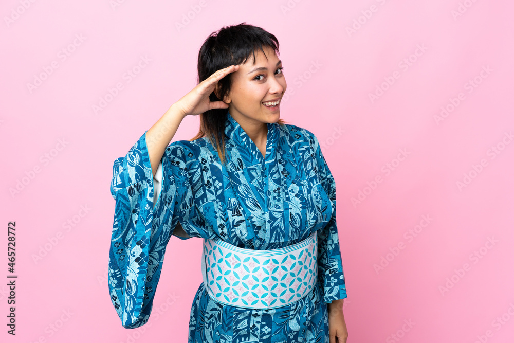 Young woman wearing kimono over isolated blue background listening to something by putting hand on the ear Young woman wearing kimono over isolated blue background listening to something by putting hand on the ear