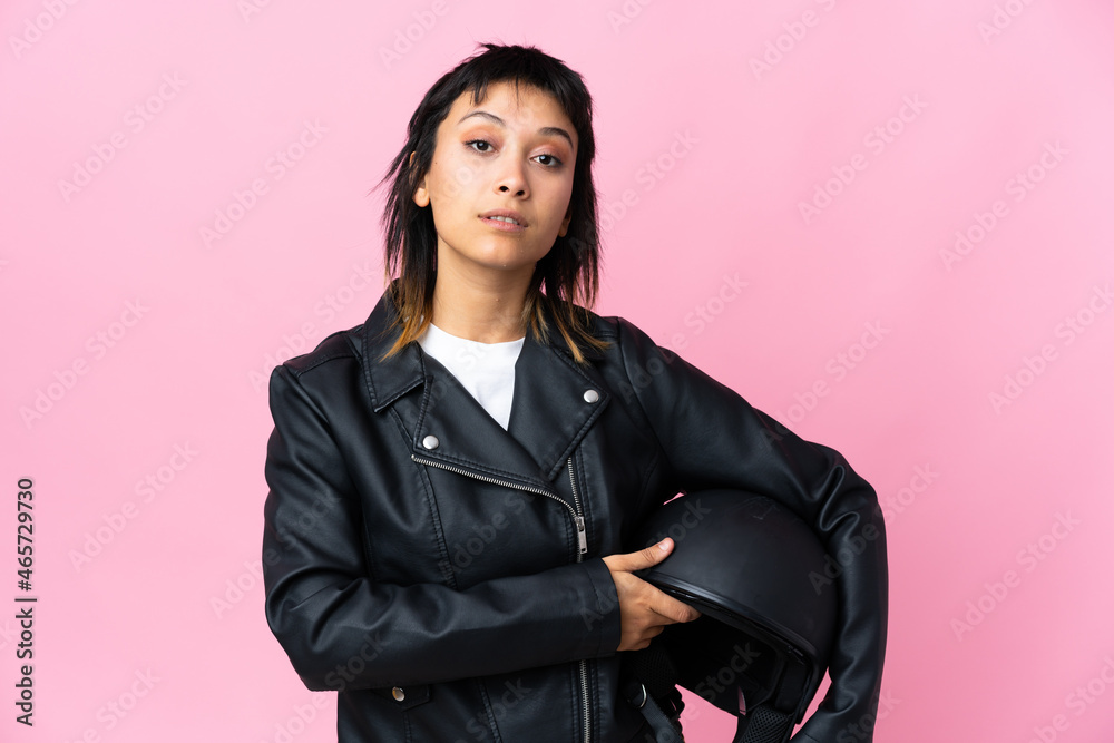 Young Uruguayan woman holding a motorcycle helmet over isolated pink background keeping arms crossed Young Uruguayan woman holding a motorcycle helmet over isolated pink background keeping arms crossed