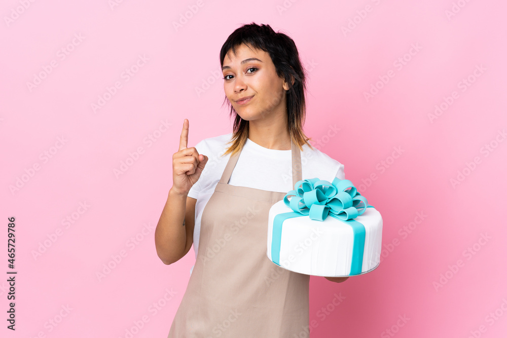 Uruguayan Pastry chef holding a big cake over isolated pink background pointing with the index finger a great idea Uruguayan Pastry chef holding a big cake over isolated pink background pointing with the index finger a great idea