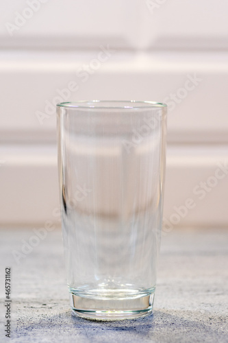 Large empty transparent glass standing on a blue wooden table in the kitchen. A glass of milk for breakfast.