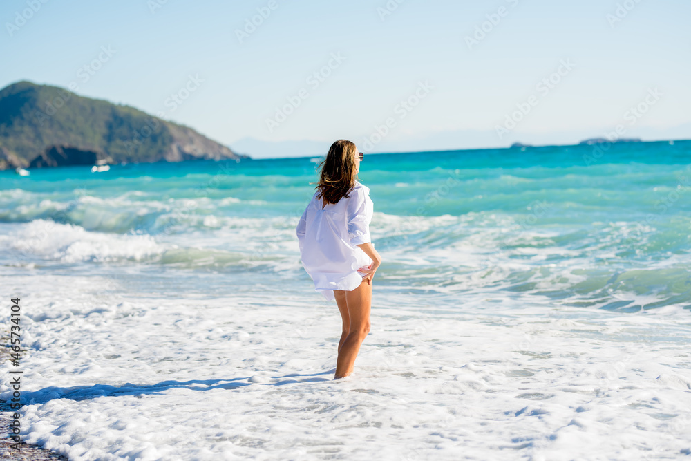 A girl with wet hair in a white shirt in the foam of the waves against the background of the azure waves of the sea. 