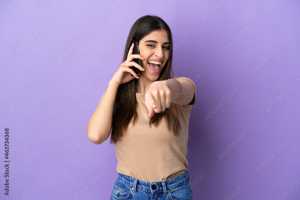 Young caucasian woman using mobile phone isolated on purple background pointing front with happy expression