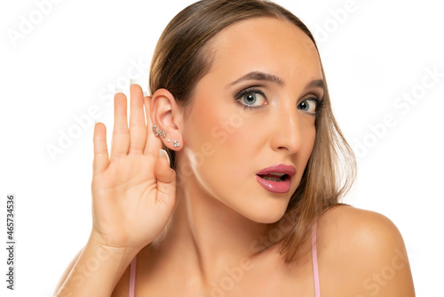 Young woman is straining a hand behind her ear while listening