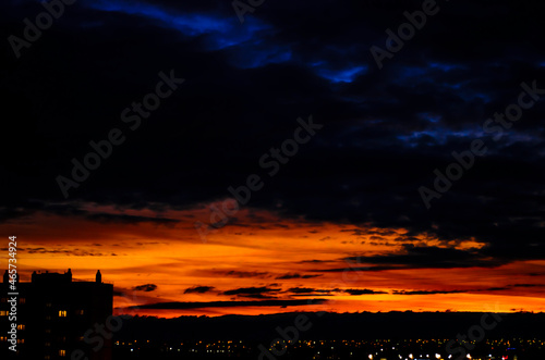 Sunset on the background of the city, beautiful dark blue sky and clouds illuminated by the sun, black silhouettes of houses