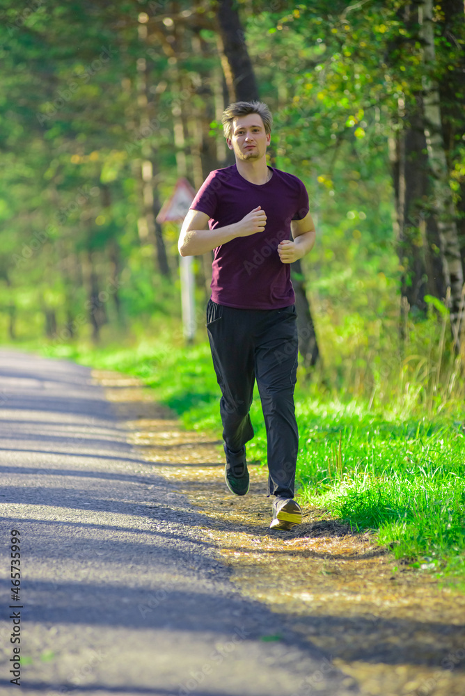Running man jogging in city park at beautiful summer day. Sport fitness model caucasian ethnicity training outdoor.