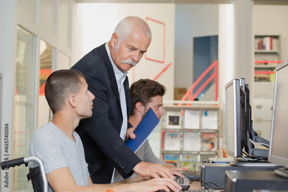 teacher helping young men using computers one in wheelchair Stock Photo ...