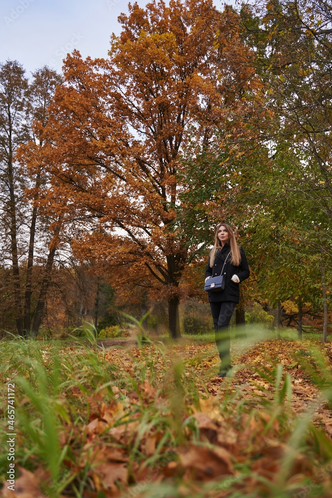 young woman with long hair and dark clothes stands in the autumn forest among foliage and yellow trees