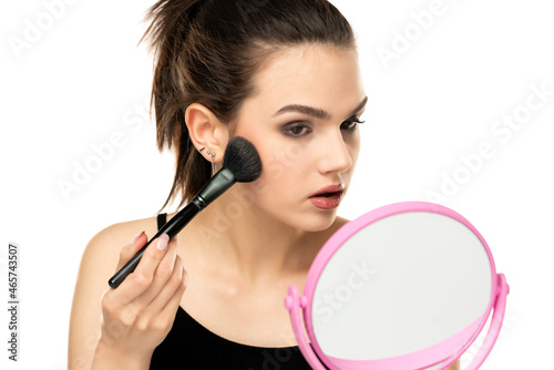 portrait of a serious teen girl applying makeup with a makeup brush on her face