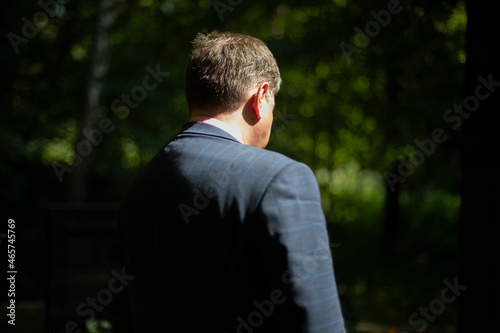 A close-up of a man on a sunny day, a view from behind. A man in a strict blue suit and a white shirt