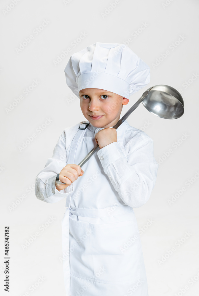 Close-up portrait of little happy boy in white cook uniform and huge chef's hat with big ladle isolated on white studio background. Close-up portrait of little happy boy in white cook uniform and huge chef's hat with big ladle isolated on white studio background.