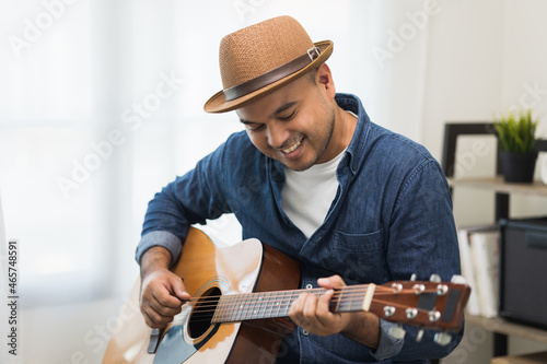 Lifestyle concept. Young asian musician playing guitar in living room at home on this weekend. Relaxing with song and music. Asian man having fun playing acoustic guitar