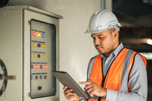 Young asian engineer working at electric cabinet checking and maintenance for the safety. Worker using tablet to control the system electric of the building.