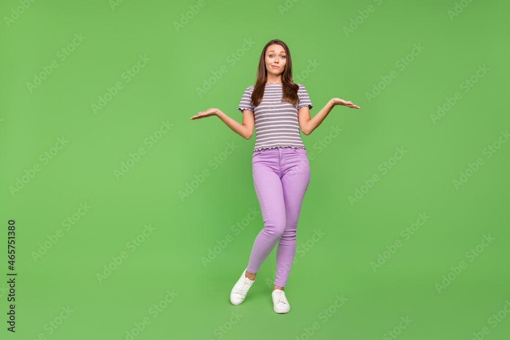 Full length photo of happy clueless young woman shrug shoulders no idea isolated on green color background Full length photo of happy clueless young woman shrug shoulders no idea isolated on green color background