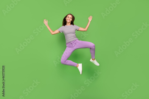 Full body photo of joyful young positive woman jump up raise hands good mood weekend shopping isolated on green color background