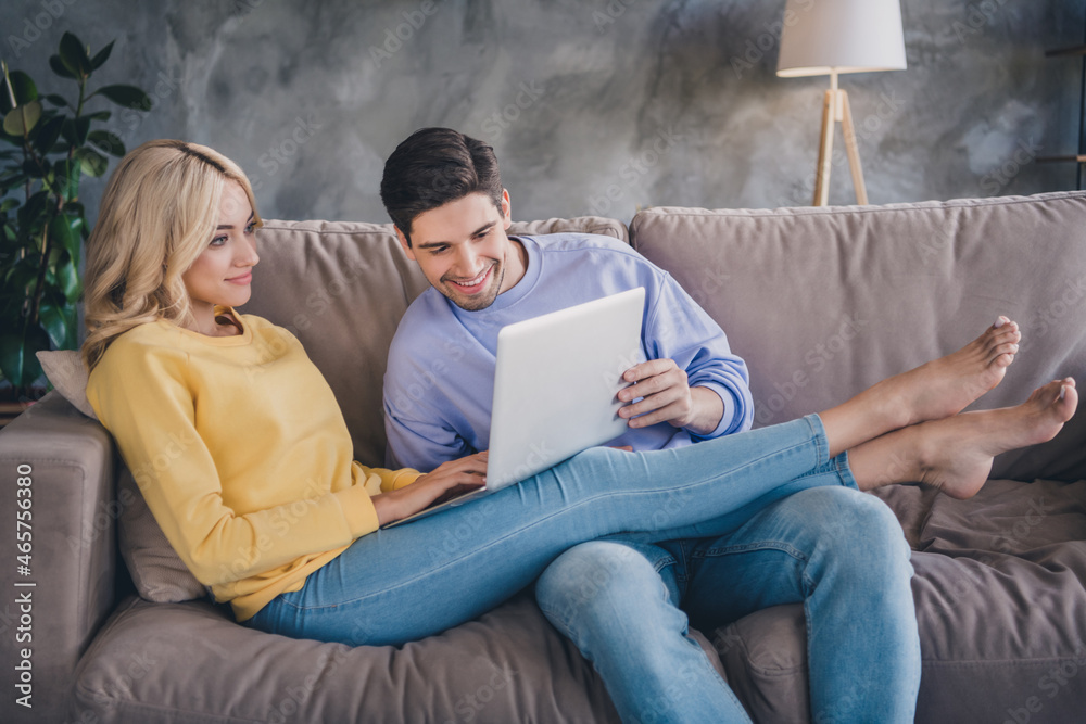 Photo of young cheerful couple happy positive smile look read browse laptop online sit couch indoors Photo of young cheerful couple happy positive smile look read browse laptop online sit couch indoors