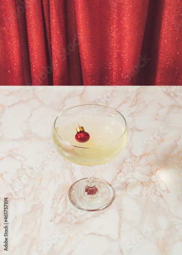 Retro vintage scene with champagne glass and Christmas bauble on marble table against shiny red curtain. Creative luxury xmas party.