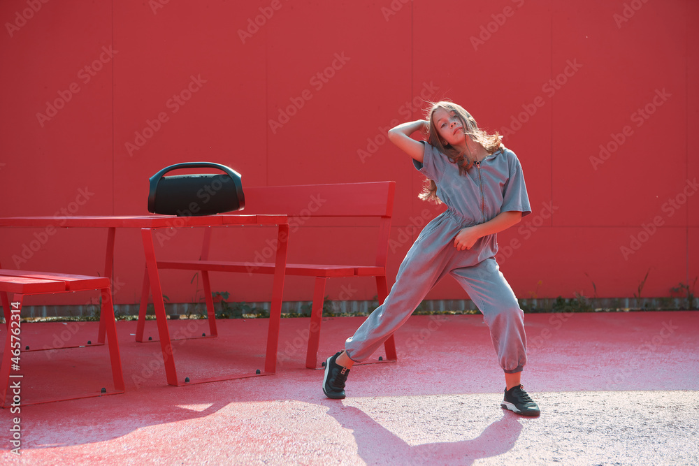 Active teen girl dancing hip hop with wireless outdoor speaker outside on red background. Dance school advertisement