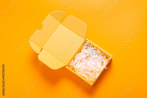 Simple yellow cardboard box on color background, empty inside with filler © mdbildes