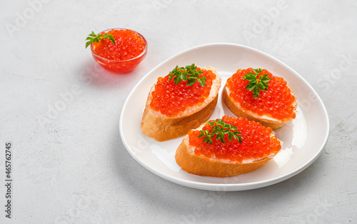Sandwiches with red caviar and fresh herbs on a gray background.