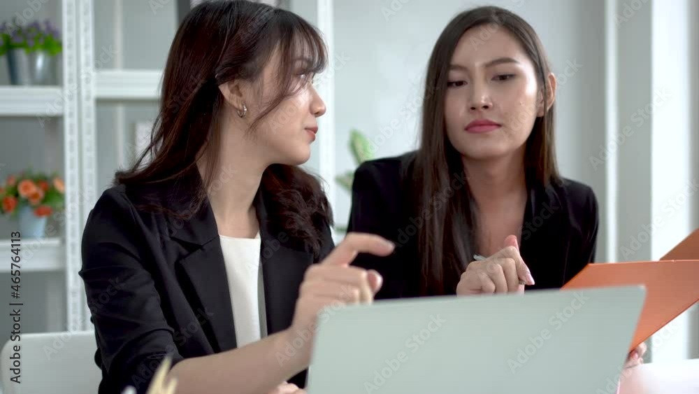An Asian businesswoman uses a laptop to search and explain information to her secretary to write down notes in a folder. An Asian businesswoman uses a laptop to search and explain information to her secretary to write down notes in a folder.