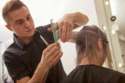 Handsome hairdresser cutting woman hair with professional scissors