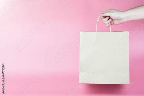 Hand holding a paper gift bag for purchase on pastel pink background. concept of prototype packaging prototype. Natural products, advertisements, delivery, and gift.