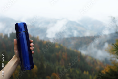 Woman holding blue thermos in mountains, closeup. Space for text