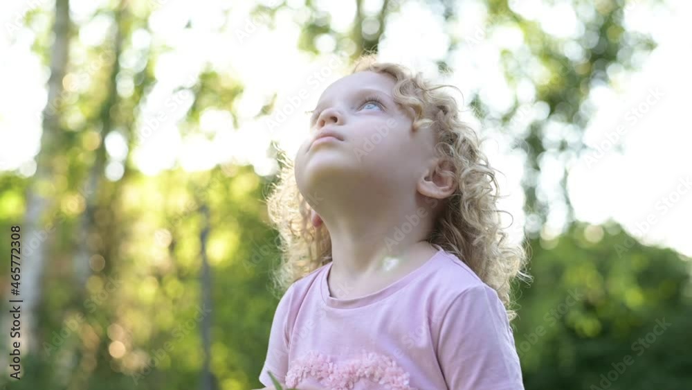 Portrait of a little beautiful curly-haired girl who looks into the sky. Slow motion Portrait of a little beautiful curly-haired girl who looks into the sky. Slow motion