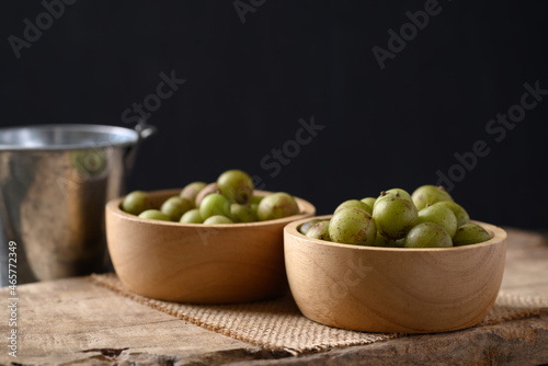 Wild Indian gooseberry or amla in a bowl on wooden with black background, Fruit tree in Asia use in various cuisine, herbal medicine and rich vitamin C