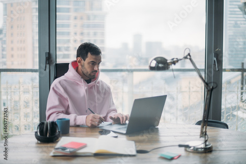 A young man works alone in the office with a laptop. Handsome guy sits at a table, works at a computer