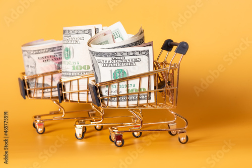 Shopping carts with dollars paper bills on a yellow background. Financial concept.