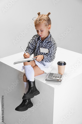 Cropped portrait of cute little girl making notes, countng isolated over gray background photo